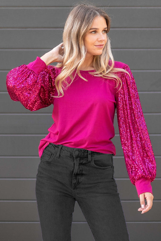 A woman wearing a magenta solid top with sequin sleeves and black trousers.